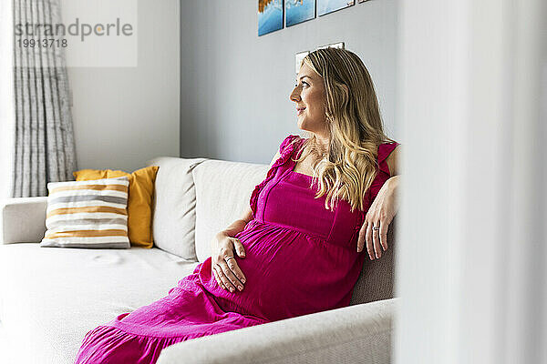 Contemplative pregnant woman sitting on sofa at home