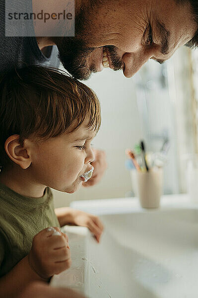 Father helping son to brush teeth in bathroom at home