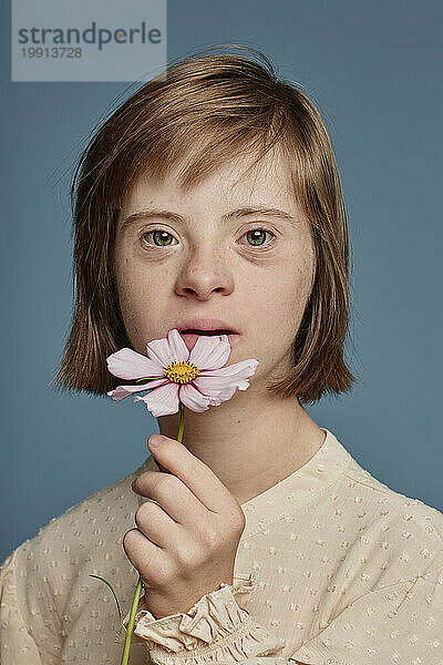 Mädchen mit Down-Syndrom hält rosa Blume vor blauem Hintergrund