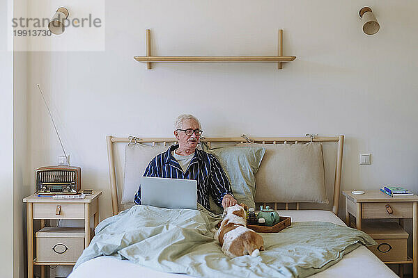 Älterer Mann sitzt mit Laptop und streichelt Hund zu Hause