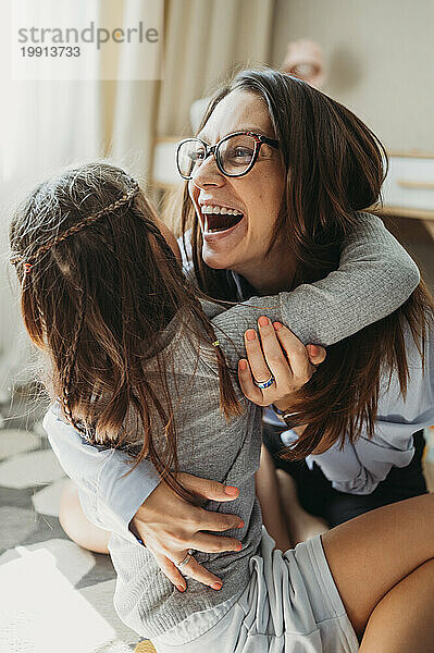 Mutter umarmt Tochter und lacht zu Hause