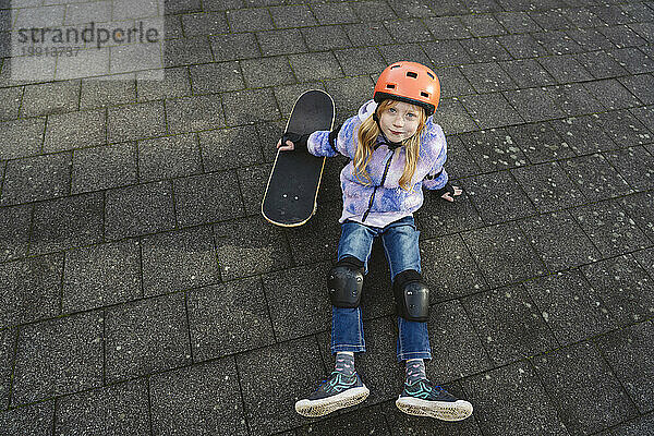 Mädchen sitzt neben Skateboard auf dem Boden