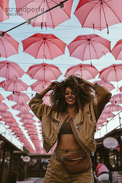 Smiling woman standing with hand in hair under pink umbrellas