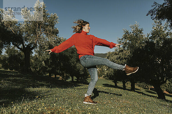Verspielte Frau tanzt an einem sonnigen Tag im Olivenfeld