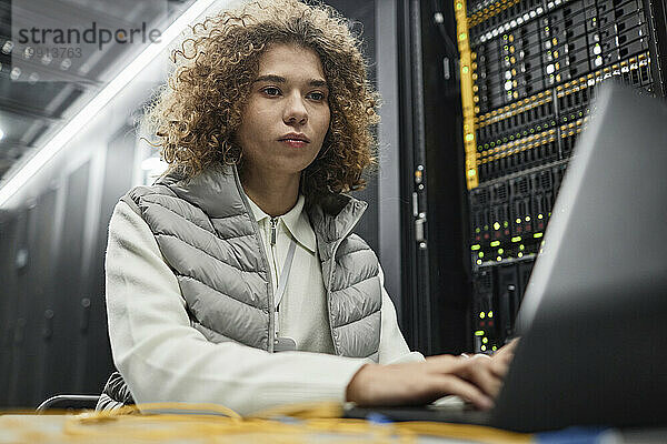 Ingenieur mit lockigem Haar arbeitet am Laptop im Serverraum