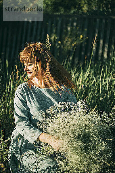 Junge Frau mit Blumen kauert im Feld