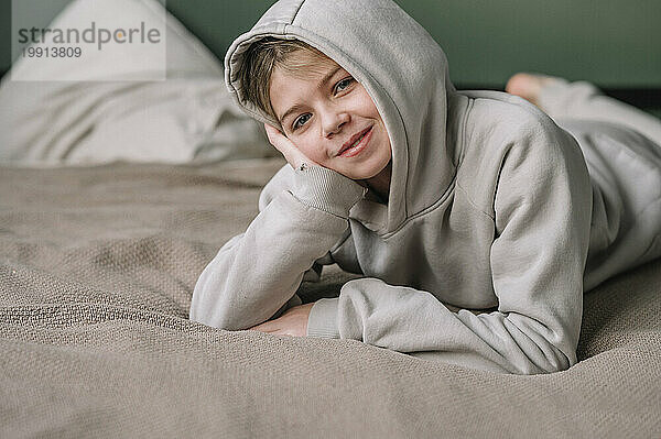 Smiling girl wearing hooded shirt and lying on bed at home
