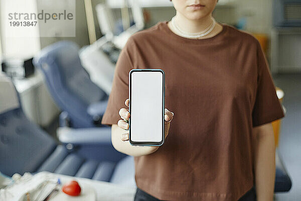Frau zeigt leeres Smartphone-Display im Blutspendezentrum