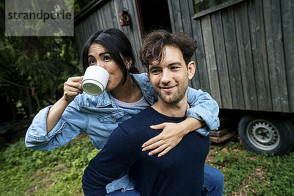 Lächelnder junger Mann fährt huckepack mit einer Frau  die Kaffee trinkt