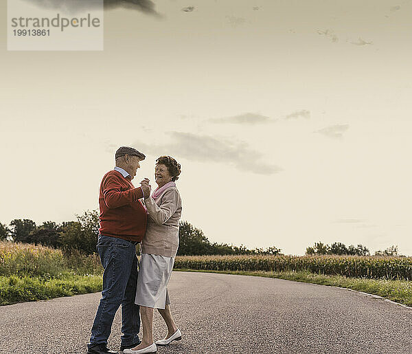 Happy senior couple dancing on road under sky