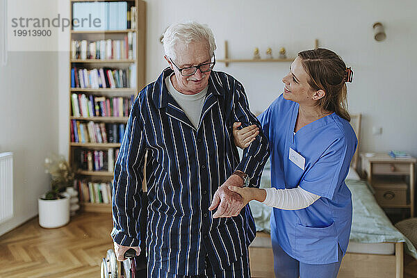 Lächelnder Mitarbeiter im Gesundheitswesen  der sich zu Hause um einen älteren Mann kümmert