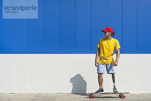 Junger Mann mit Behinderung steht auf Skateboard an der Wand