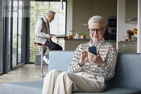 Ältere Frau sitzt zu Hause auf der Couch und benutzt ihr Mobiltelefon