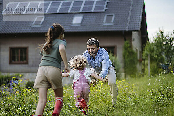 Vater und Töchter vergnügen sich vor ihrem Familienhaus mit Sonnenkollektoren auf dem Dach