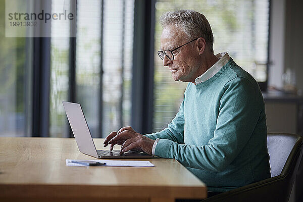 Älterer Mann benutzt Laptop am Tisch zu Hause