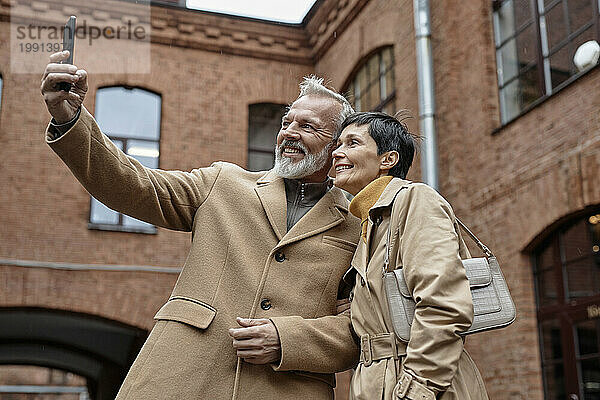 Happy elderly couple taking selfie on smartphone during city walk