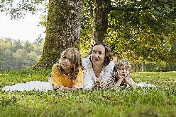 Mother lying down with son and daughter on grass at park