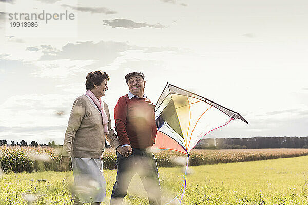 Happy senior couple holding hands and walking with kite at field