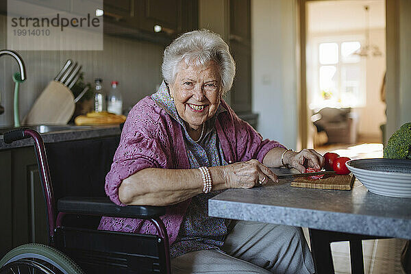 Glückliche Seniorin schneidet Tomaten mit Messer in der heimischen Küche