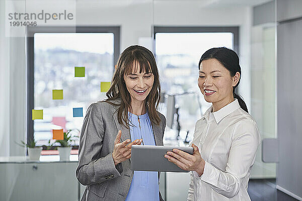 Glückliche Geschäftsfrauen diskutieren gemeinsam über Tablet-PC im Büro