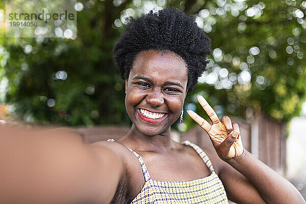 Lächelnde Frau gestikuliert mit einem Friedenszeichen und macht ein Selfie