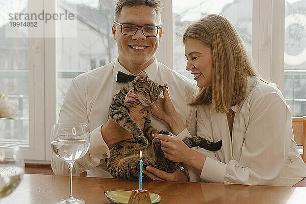 Happy man and woman holding and petting cat at home