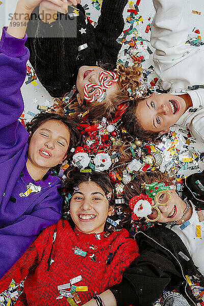 Happy friends lying near Christmas decorations on floor
