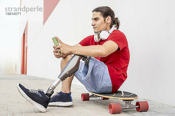 Nachdenklicher Mann mit Behinderung sitzt auf Skateboard