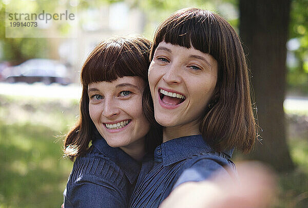 Glückliche Zwillingsschwestern machen Selfie im Park