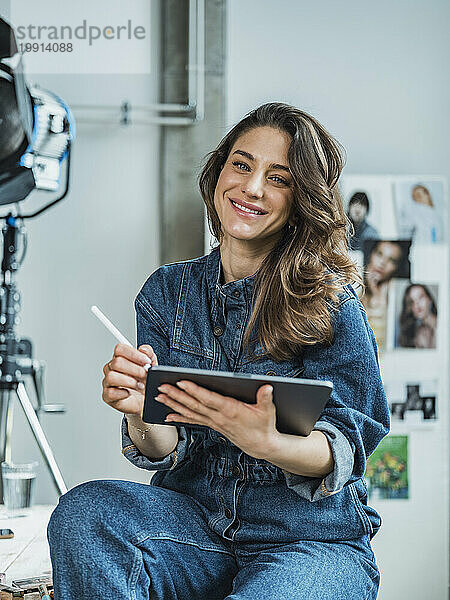 Lächelnder Influencer sitzt mit Tablet-PC und digitalisiertem Stift im Studio