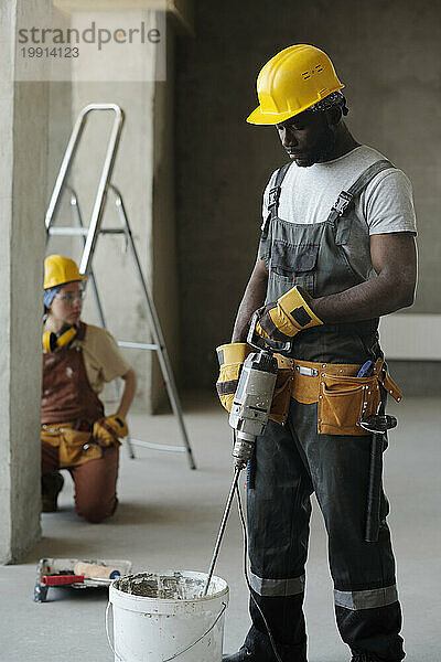 Bauarbeiter mischt vor Ort Zement mit Werkzeug im Eimer