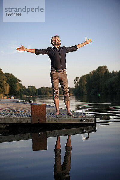 Man standing with arms outstretched on jetty near lake