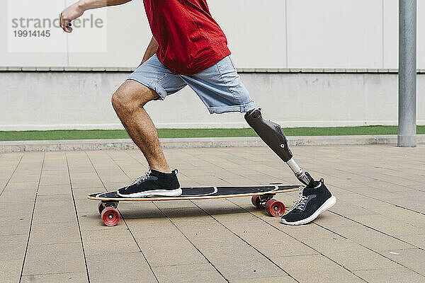 Mann mit Beinprothese fährt Skateboard am Fußweg