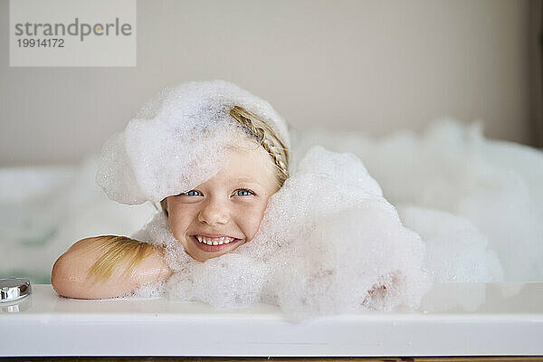 Lächelndes Mädchen mit Seifenlauge in der Badewanne bedeckt