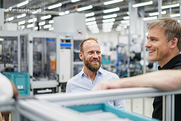 Lächelnder Geschäftsmann blickt Mitarbeiter in einer Fabrik an