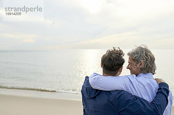 Glücklicher Vater und Sohn mit Arm umeinander am Strand