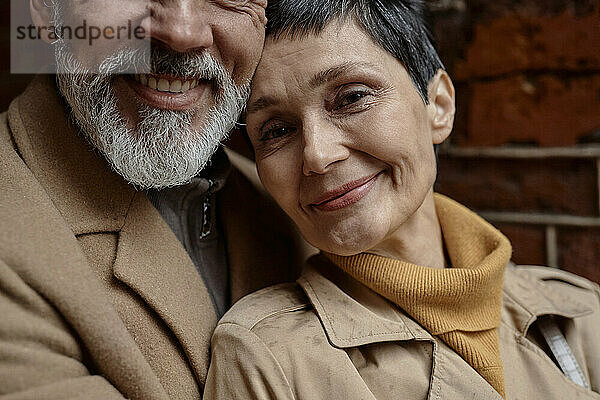 Positive adult woman leaning on her husband and looking at camera