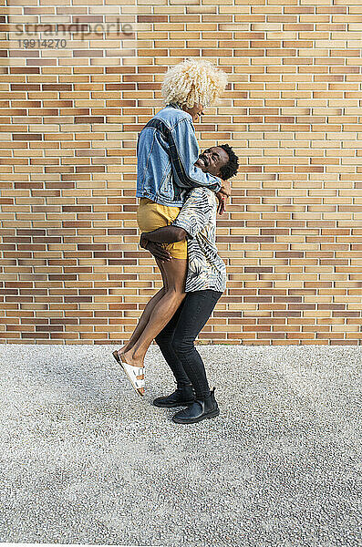 Boyfriend lifting transgender woman standing in front of brick wall
