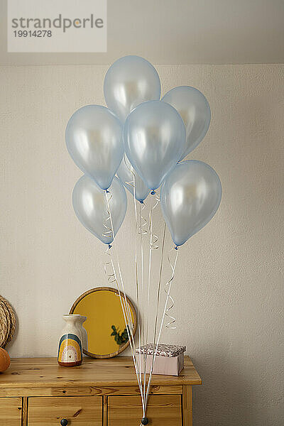 Balloons and gift box on cabinet at home