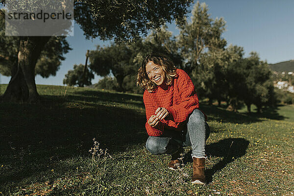 Frau kauert und lacht an einem sonnigen Tag im Olivenfeld