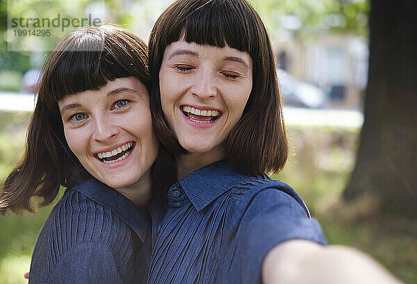 Cheerful twin sisters taking selfie in park
