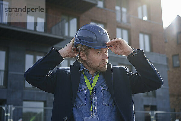 Architect adjusting hardhat in front of buildings on sunny day