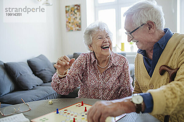 Fröhliche Frau spielt Ludo mit Mann am Tisch im Wohnzimmer