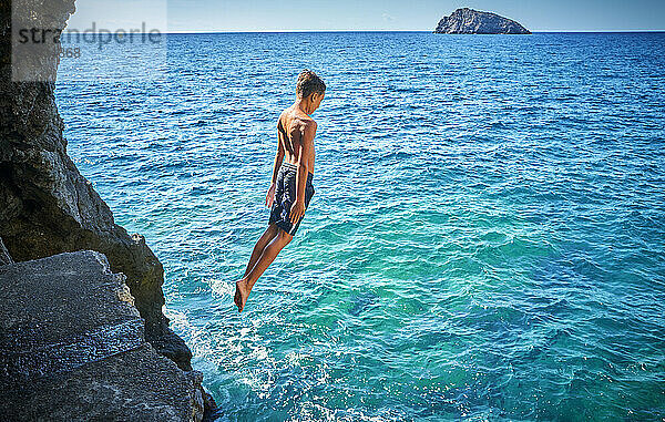 Junge springt von einer Klippe im blauen Meer