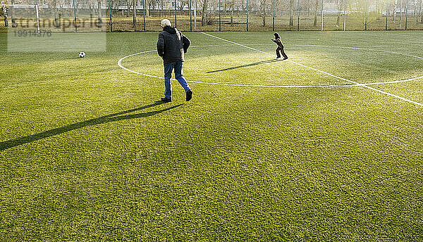Großvater und Enkel laufen dem Ball auf dem Fußballplatz hinterher