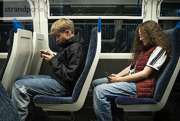 Boy and girl using smart phones sitting in train