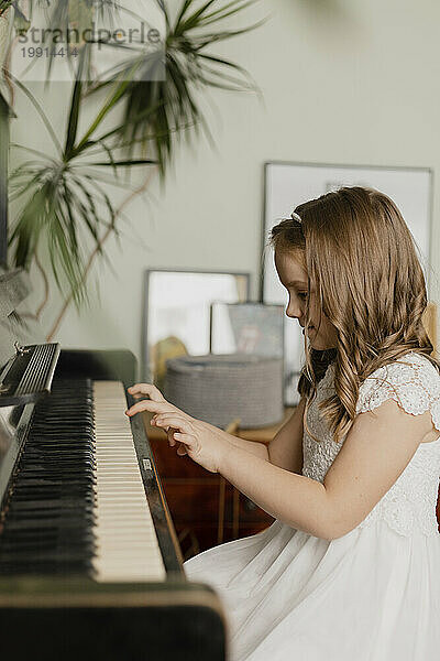Mädchen trägt weißes Kleid und spielt zu Hause Klavier