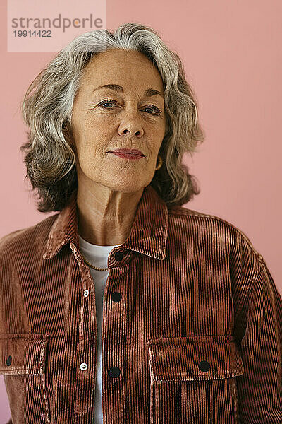 Ältere Frau trägt Cordjacke vor rosa Hintergrund
