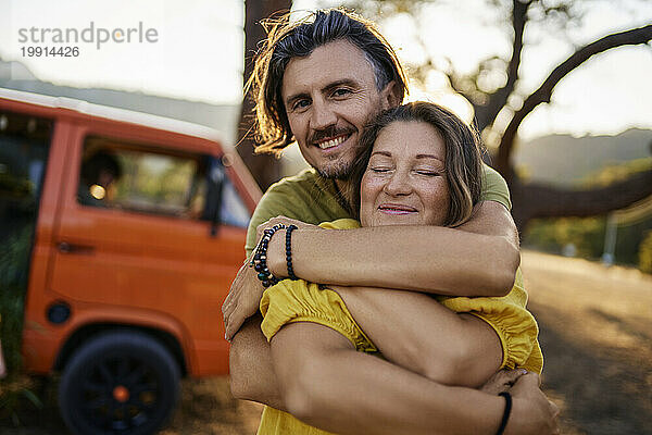 Lächelnder Mann umarmt Freundin  die neben Wohnwagen steht