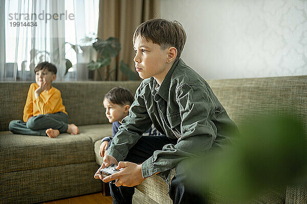 Boy playing video game with siblings at home